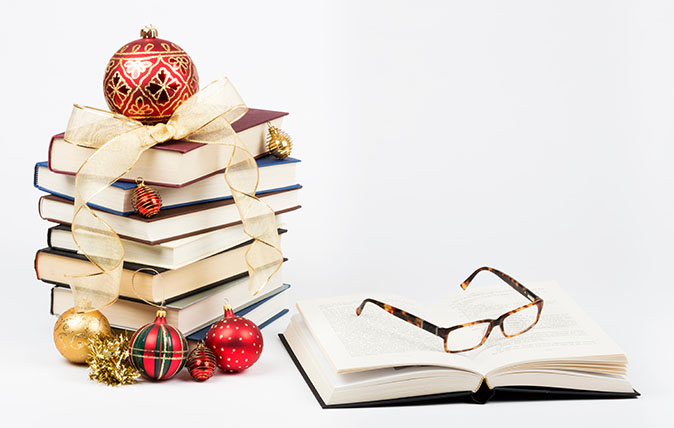 Gift of knowledge concept with a pile of books and reading glasses with Christmas ornaments